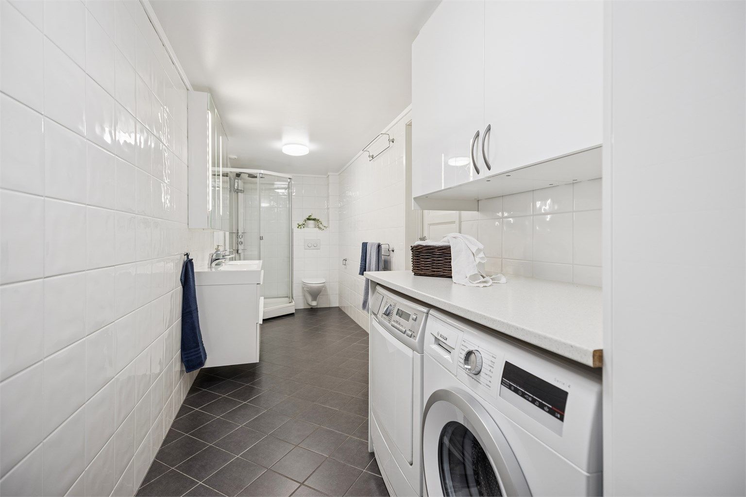 Pent flislagt bad/vaskerom i underetasjen med dobbel servantinnredning, dusjkabinett, vegghengt toalett og opplegg for vaskemaskin og tørketrommel.