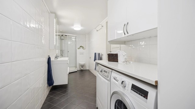 Pent flislagt bad/vaskerom i underetasjen med dobbel servantinnredning, dusjkabinett, vegghengt toalett og opplegg for vaskemaskin og tørketrommel.