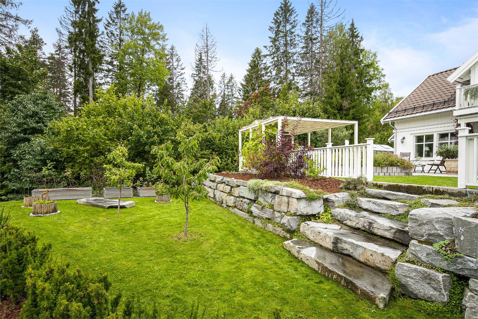 Tomten er opparbeidet i nivåer med solide forstøtningsmurer og trapper i naturstein.