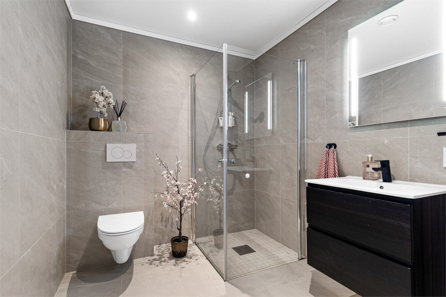 Bad fra byggeår. Flislagt gulv med varme og flislagte vegger. Nedsenket himling med downlights. Vegghengt servantskap med ovenpåliggende servant og ett-greps armatur.