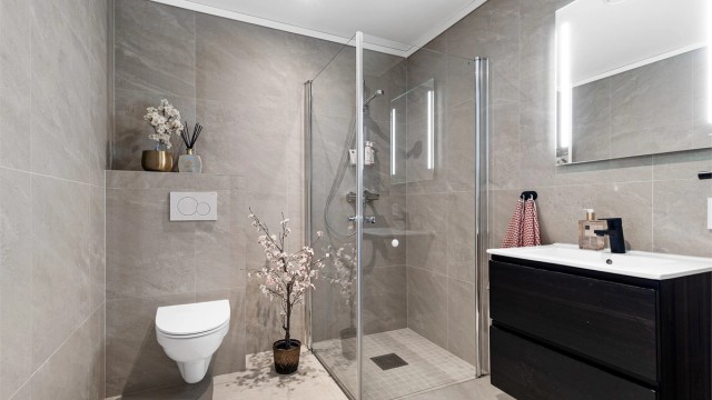 Bad fra byggeår. Flislagt gulv med varme og flislagte vegger. Nedsenket himling med downlights. Vegghengt servantskap med ovenpåliggende servant og ett-greps armatur.