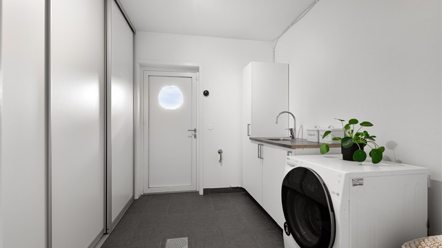 Vaskerom med flislagt gulv, opplegg for vaskesøyle, skyvedørsgarderobe og egen utgangsdør.