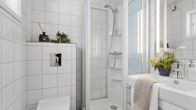 Ved entré har man bad 1 i boligen.
Helfliset bad med mørke fliser på gulv og lyse på vegg. Det er varmekabler i gulv. Vegghengt toalett, dusjkabinett, servant med skuffer. Speil på vegg med innfelt lys