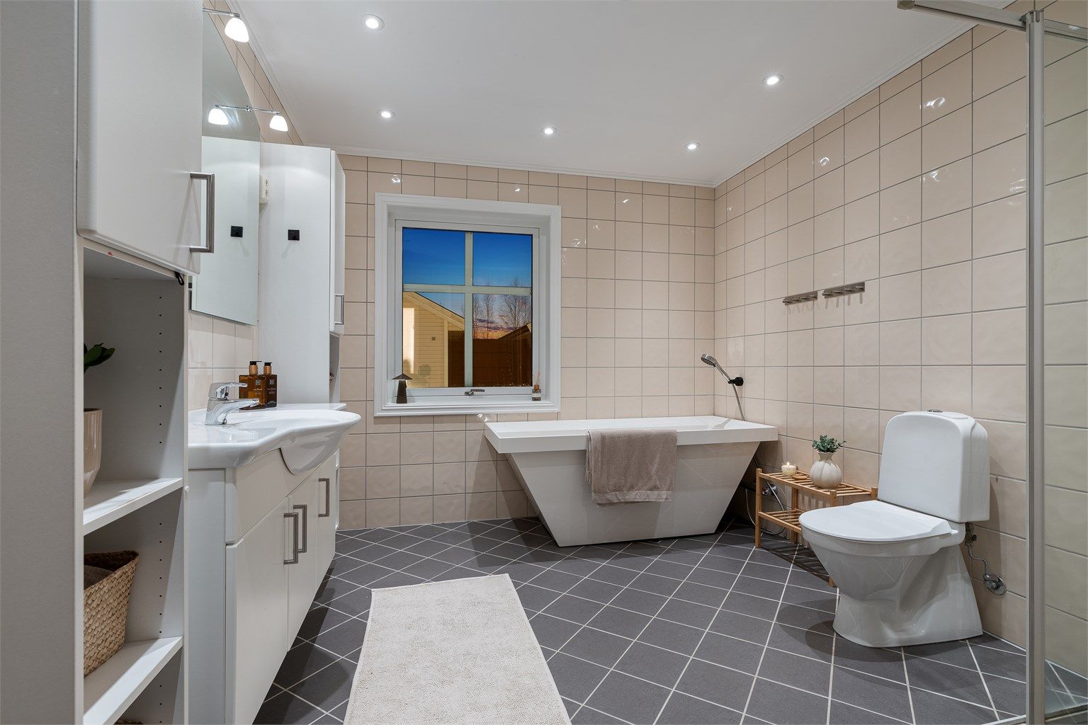 Stort flislagt bad med både frittstående badekar og dusjhjørne.