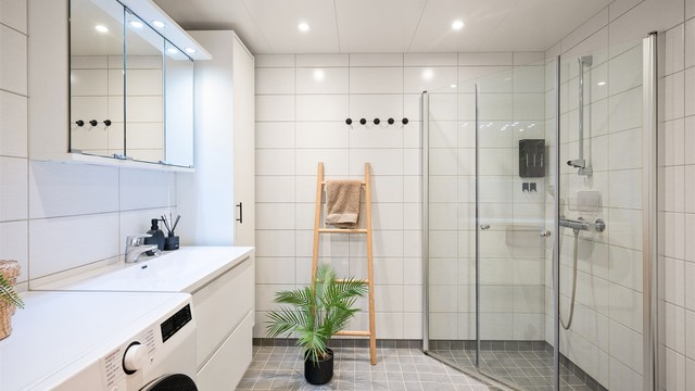 Innbydende og meget romslig bad med hvite fliser på vegg, gråmelerte fliser med varme i gulv og downlights i himling