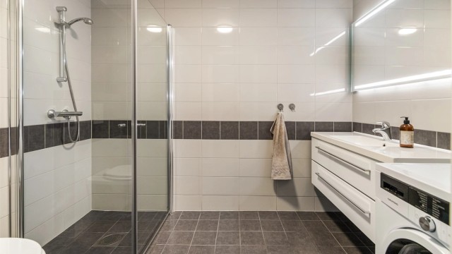 Flislagt bad/vaskerom med elektriske varmekabler, dusjhjørne og vegghengt klosett.
