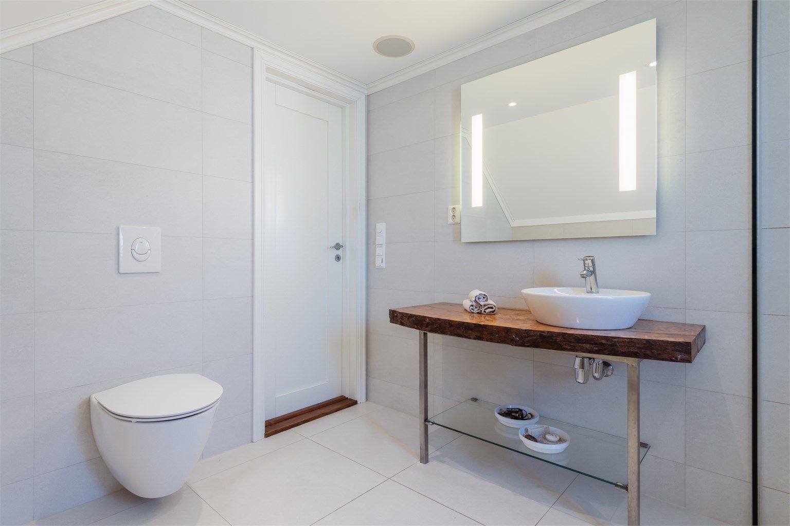 Badet er innredet med vegghengt toalett og en servant på en benkeplate av heltre.