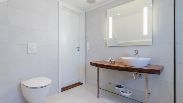 Badet er innredet med vegghengt toalett og en servant på en benkeplate av heltre.