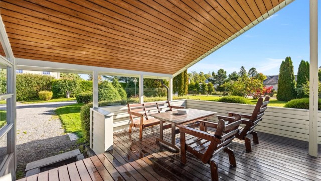 Overbygd terrasse med god plass til sittegruppe og utsyn mot hagen.