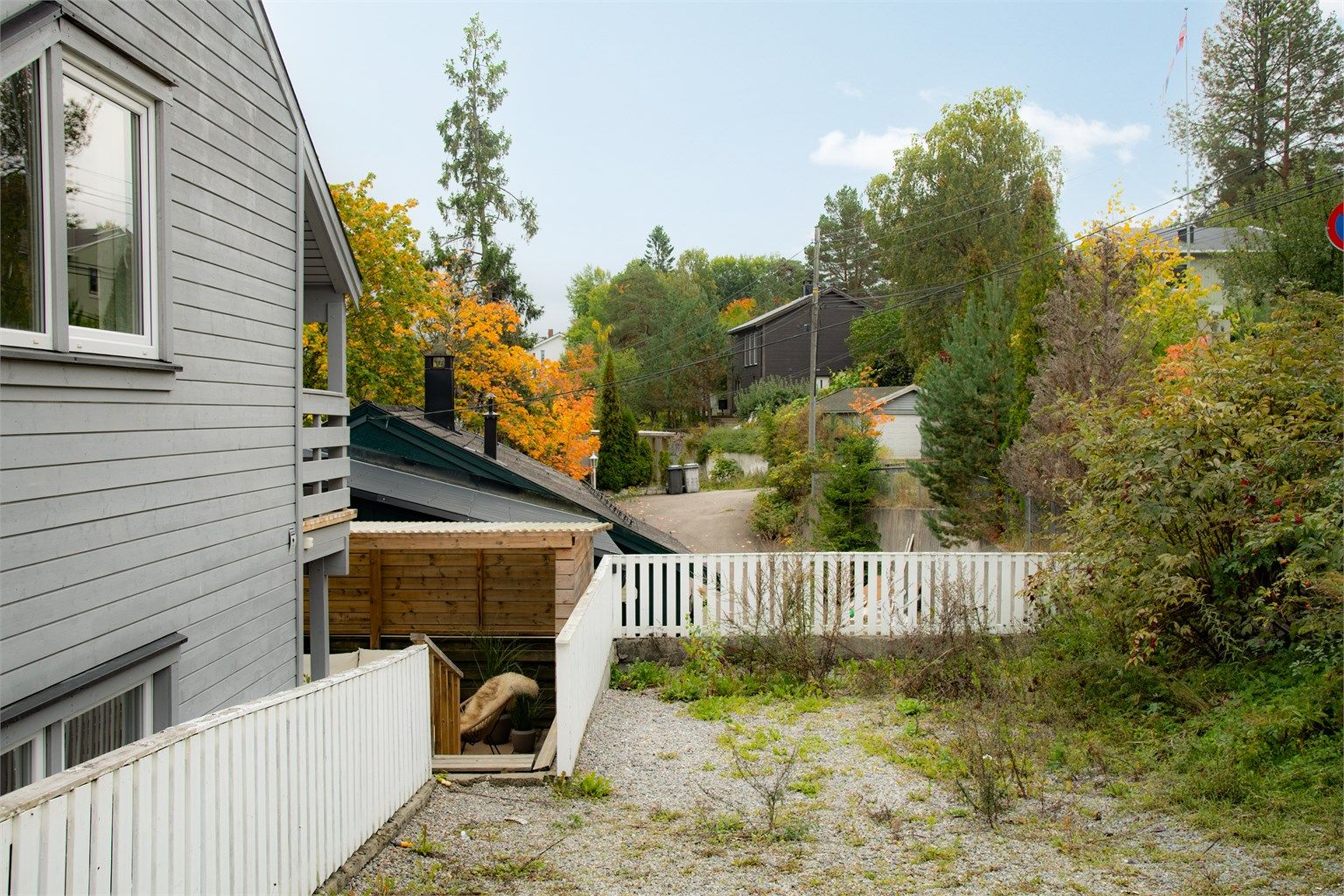 Tomten har gruset gårdsplass, hvitmalt gjerde og adkomst til utvendig bod.