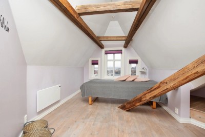 Soverom i loftetasjen med 1-stavs heltrebord på gulv, malte vegger og malt himling (synlige takbjelker)