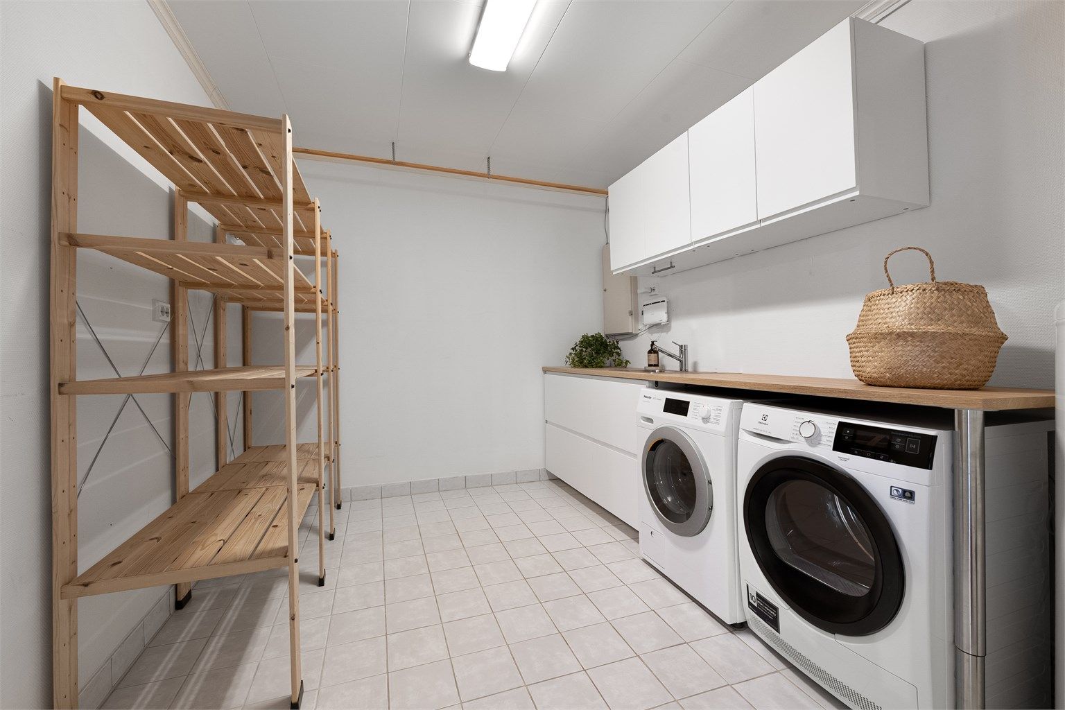 Eget vaskerom med flislagt gulv, utslagsvask og opplegg for vaskemaskin og tørketrommel.