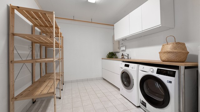Eget vaskerom med flislagt gulv, utslagsvask og opplegg for vaskemaskin og tørketrommel.