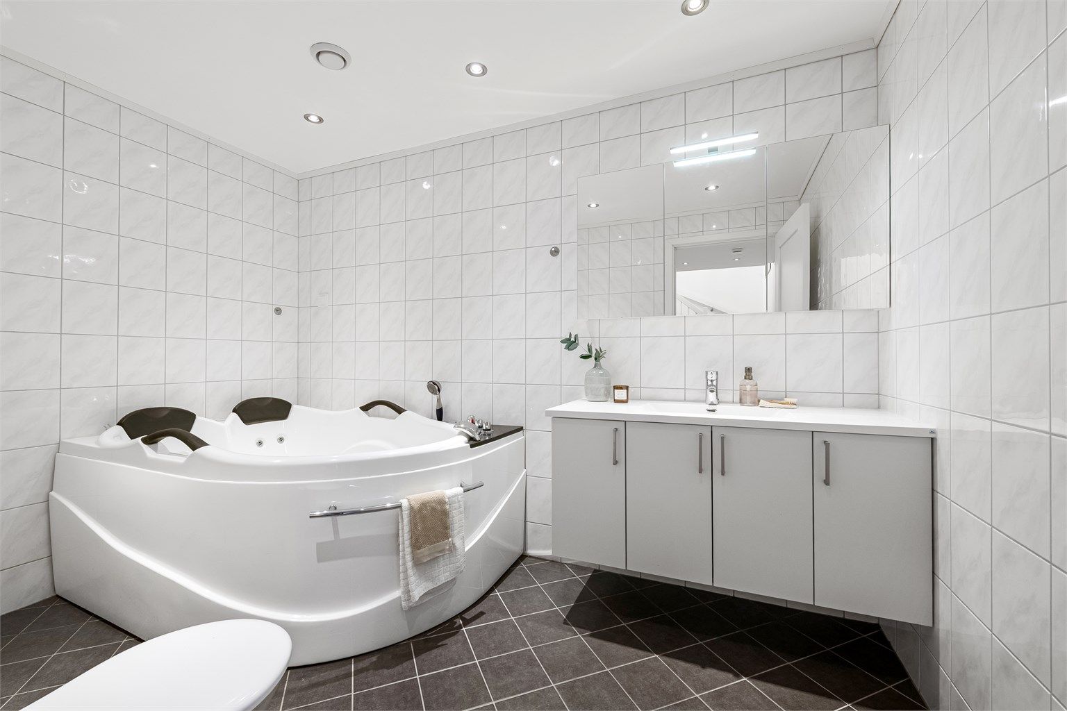 Flislagt bad i underetasjen med gulvvarme, nedsenket himling med downlights og hjørnebadekar.