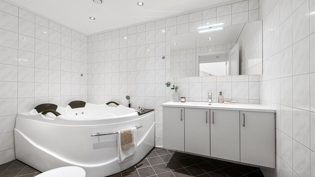 Flislagt bad i underetasjen med gulvvarme, nedsenket himling med downlights og hjørnebadekar.