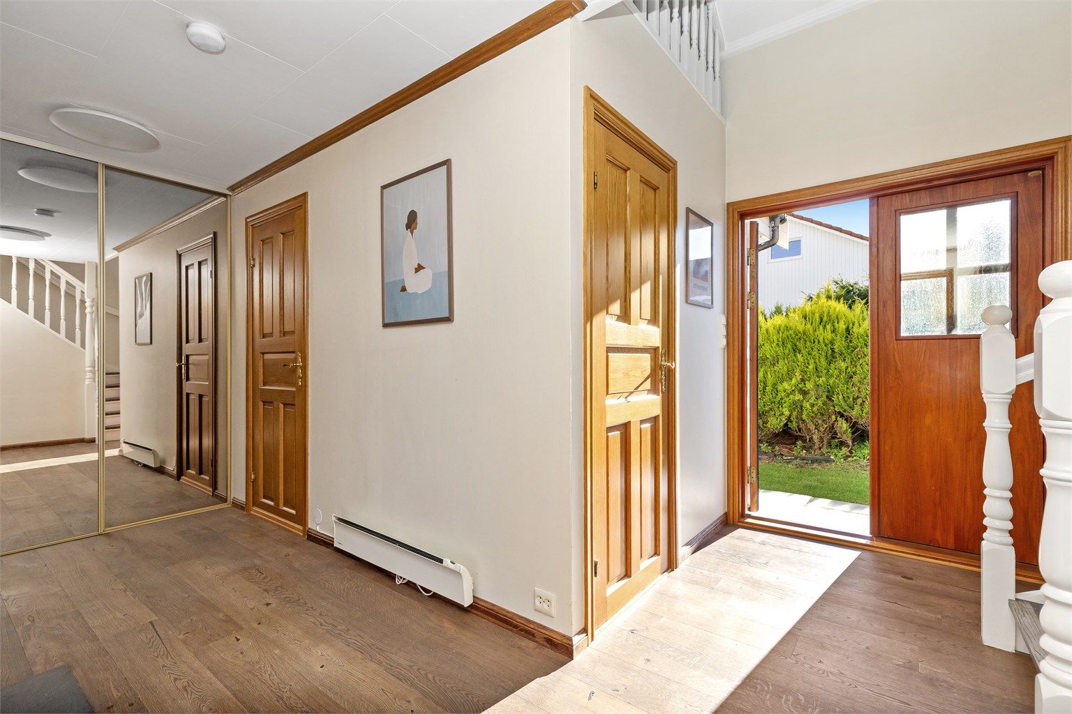 Inngangspartiet leder inn til en lys hall med skyvedørsgarderobe med speilfronter.