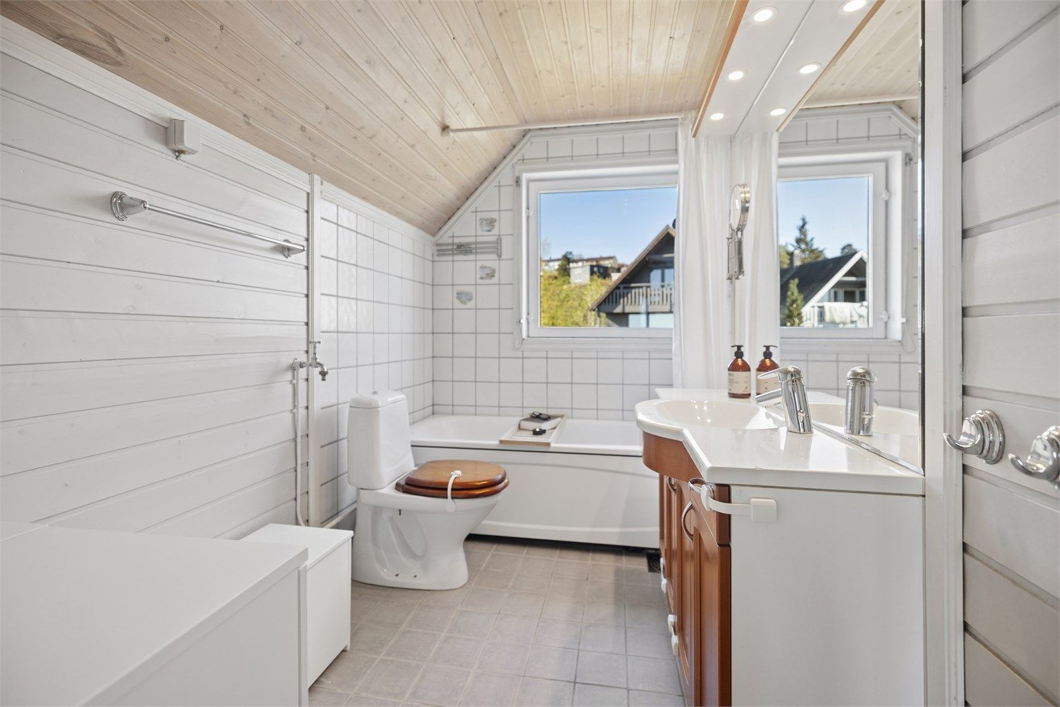 Romslig baderom med flislagt gulv og behagelig gulvvarme. Badet er innredet med badekar med veggmontert hånddusj, servantinnredning og gulvstående toalett.