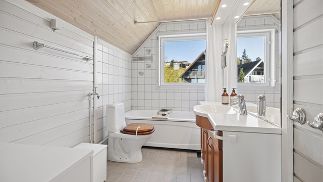 Romslig baderom med flislagt gulv og behagelig gulvvarme. Badet er innredet med badekar med veggmontert hånddusj, servantinnredning og gulvstående toalett.