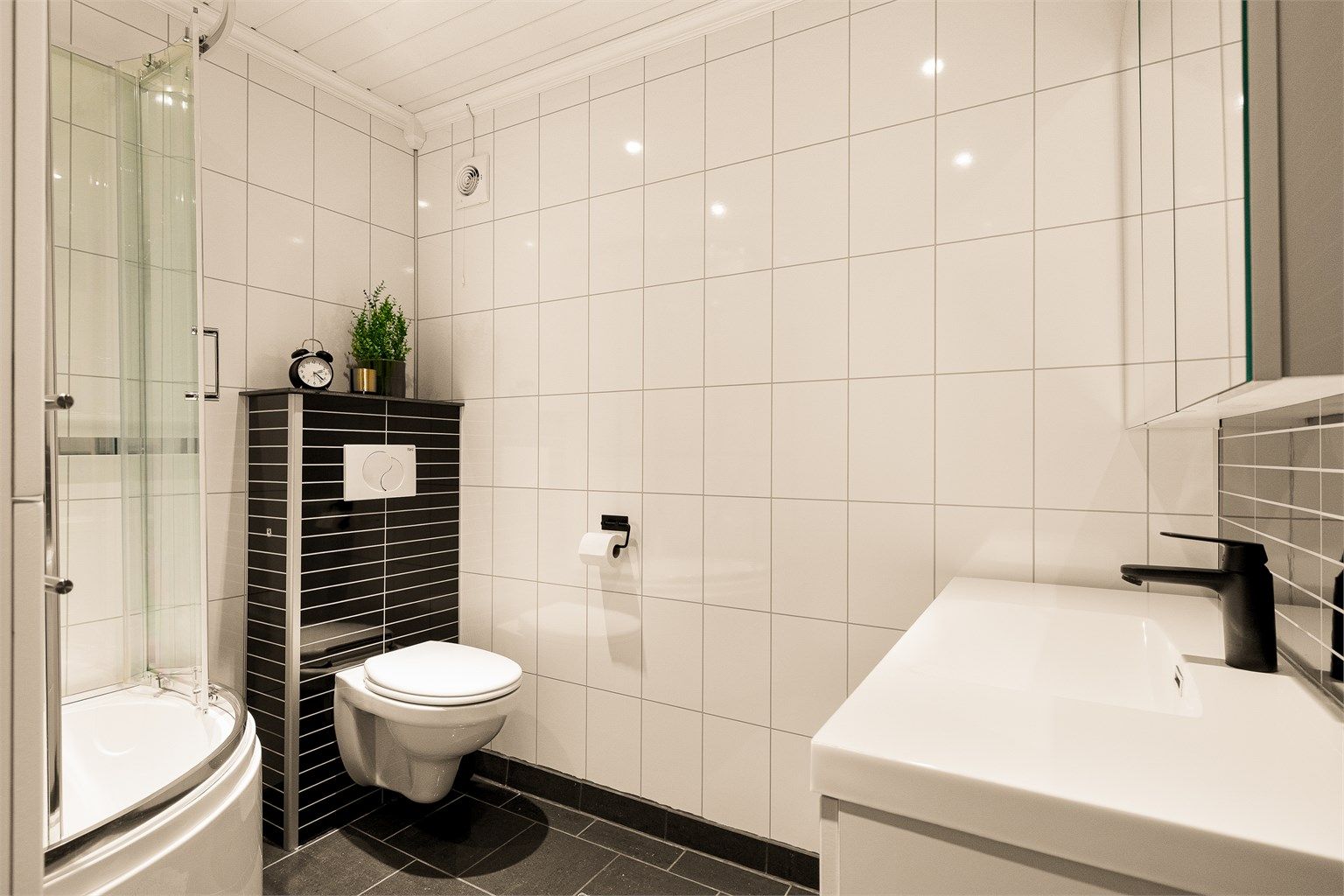 FUNKSJONELT: Baderommet er enkelt og minimalistisk med flislagt gulv og er utstyrt med wc, dusjbadekar og servant i seksjon med speilskap over.