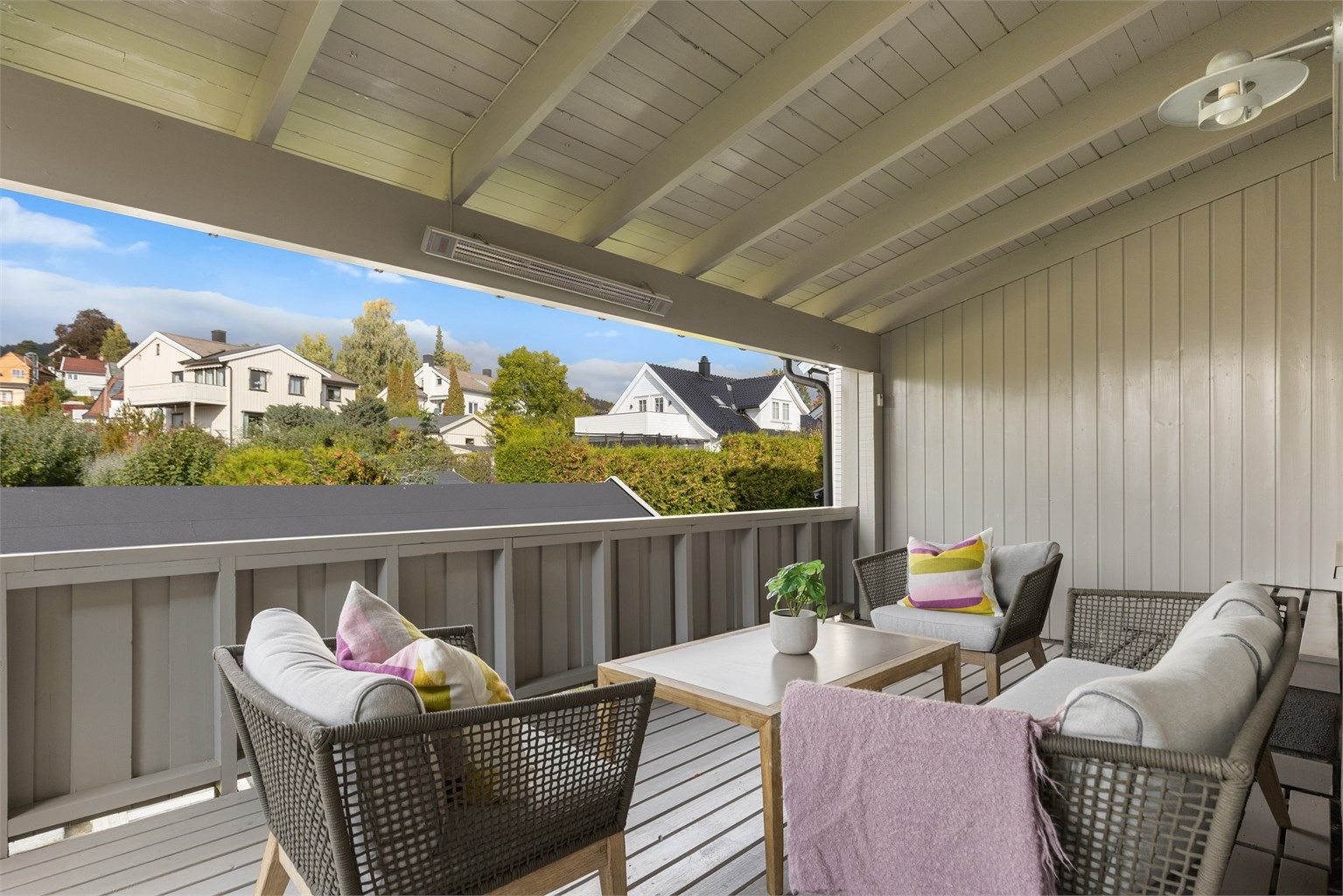Overbygd terrasse i 2. etasje med dekke av terrassebord, varmeelementer og sittegruppe.