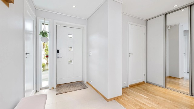 Inngangspartiet har dels flislagt gulv med varmekabler og dels parkett, hvite profilerte innerdører og en romslig skyvedørsgarderobe med dels speilfront