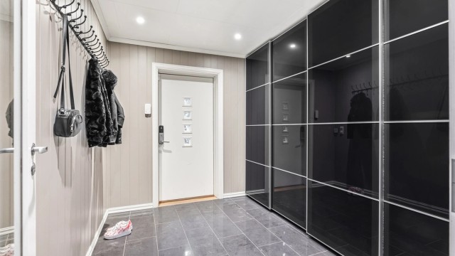 Romslig entré med mørke gulvfliser og gulvvarme. En bred skyvedørsgarderobe med sotede fronter gir utmerket oppbevaring.