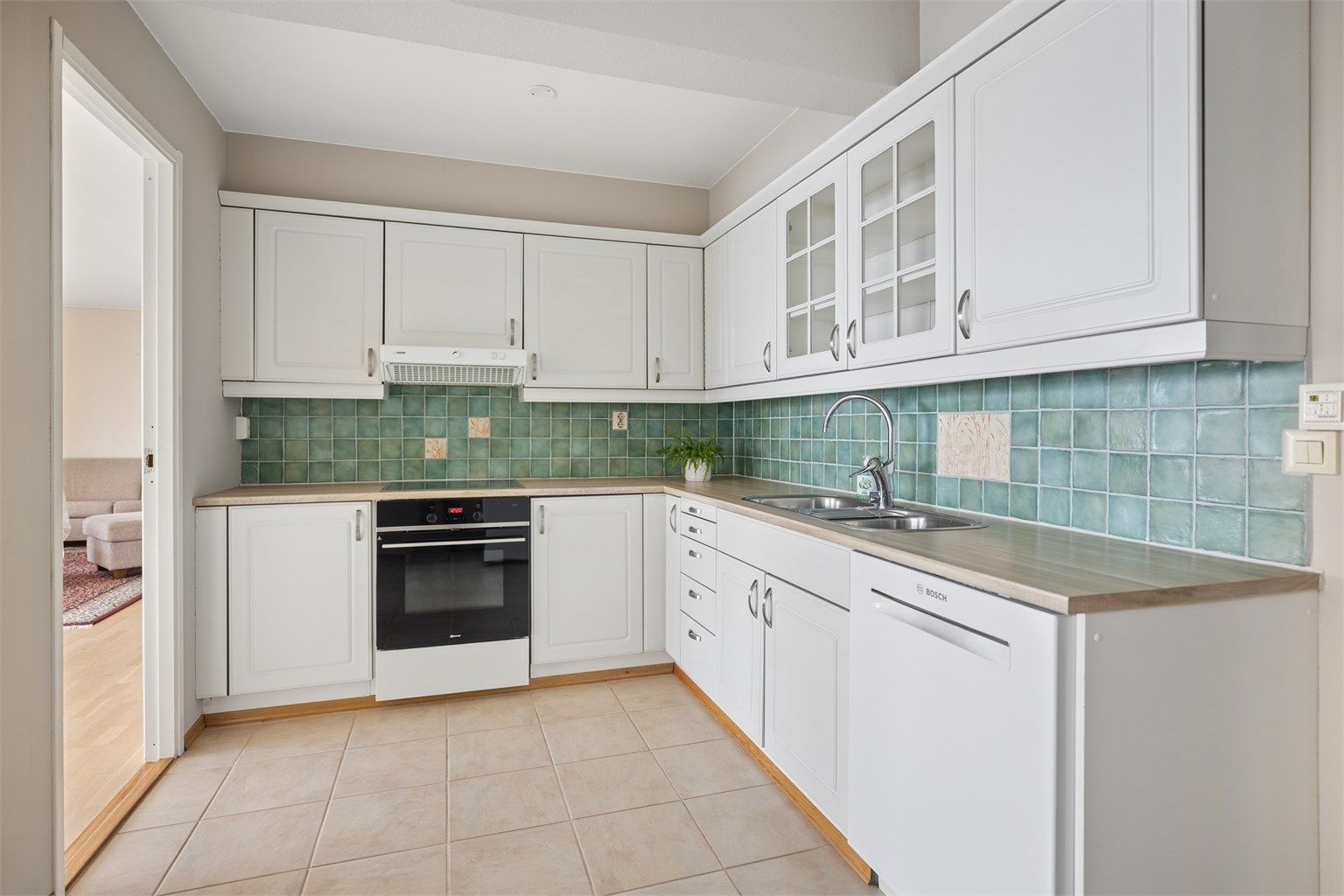 Kjøkkeninnredningen fremstår både pen og funksjonell, med rikelig benkeplass og gode oppbevaringsmuligheter i over- og underskap. De profilerte frontene gir et klassisk preg, mens glassfronter enkelte steder tilfører en elegant visuell variasjon.