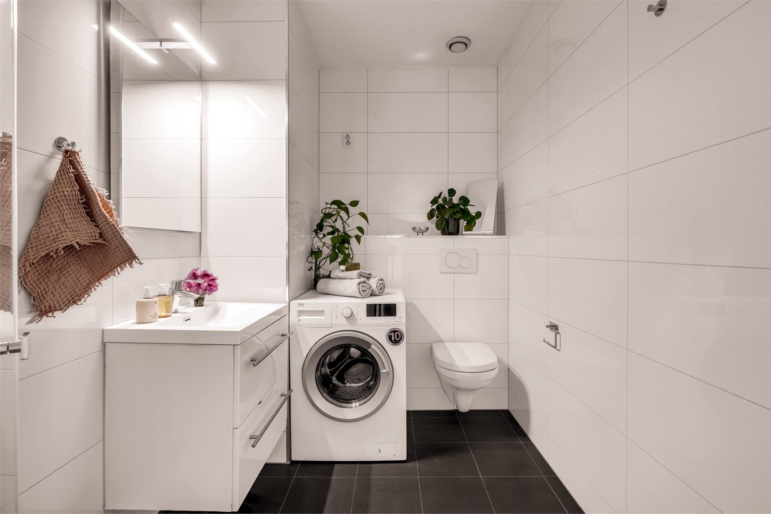 Badet er innredet med vegghengt toalett, servantinnredning med heldekkende vask og speil med lys over vasken. Det er opplegg for vaskemaskin.