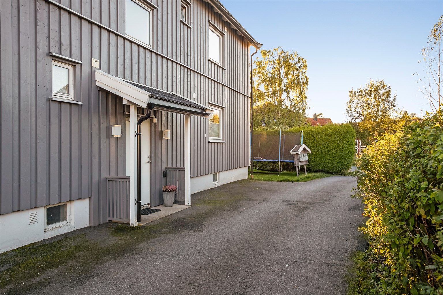 Klassisk firemannsbolig med stående trekledning og asfaltert adkomst.