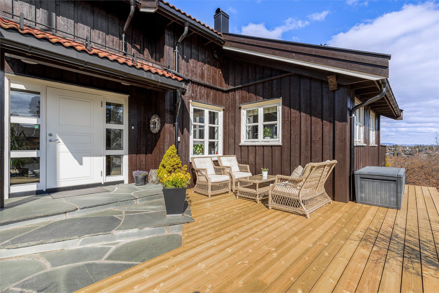 Inngangspartiet med terrasse og steinlagt trapp mot inngangsdøren.