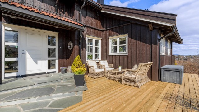 Inngangspartiet med terrasse og steinlagt trapp mot inngangsdøren.