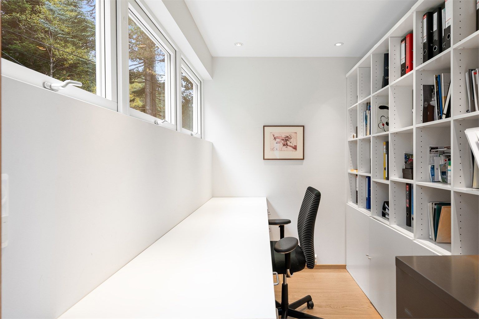 Arbeidsrom med skyvedør fra kjøkkenet, innredet med langstrakt skrivebord og bokhylle.