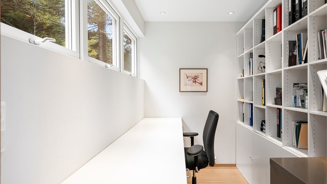 Arbeidsrom med skyvedør fra kjøkkenet, innredet med langstrakt skrivebord og bokhylle.