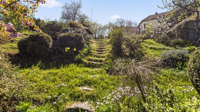 Tomten er skrånende og pent opparbeidet med plen, beplantning og trapper i naturstein.