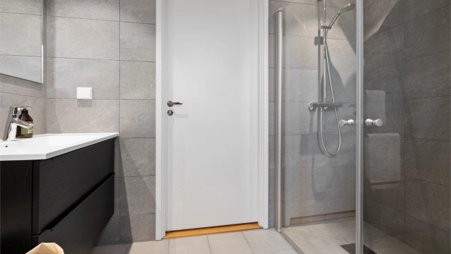 Begge badene har pene, grå fliser på veggene, downlights i himlingen og lyse fliser på gulv med elektrisk gulvvarme.