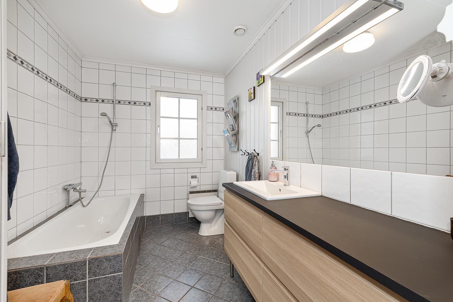 Flislagt bad med gode oppbevaringsmuligheter. Her finner du et badekar, toalett og servant med oppbevaringsmuligheter. 