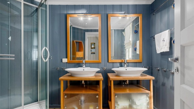 Lyst og romslig bad i 1. etasje med malte overflater og klassisk tregulv. Rommet er smakfullt innredet med to servanter med store speil, høyskap, og møblet er i solid heltre. Dusjkabinett og toalett er montert.