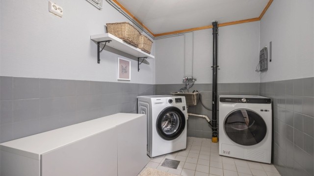Praktisk vaskerom med utslagsvask i rustfritt stål samt god plass til vaskemaskin og tørketrommel.