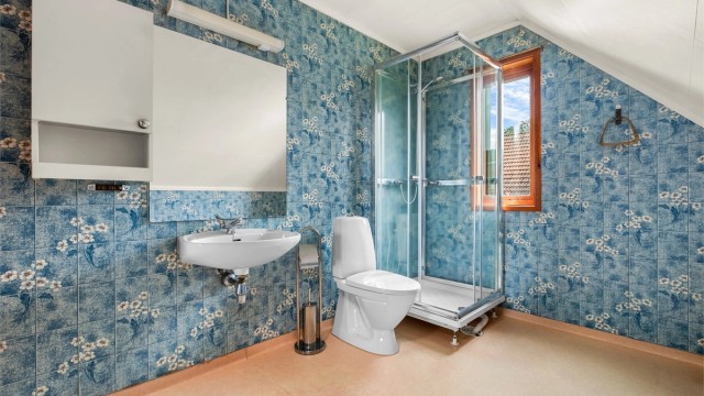 Badet er fra byggeår og er innredet med dusjkabinett, toalett og servant.