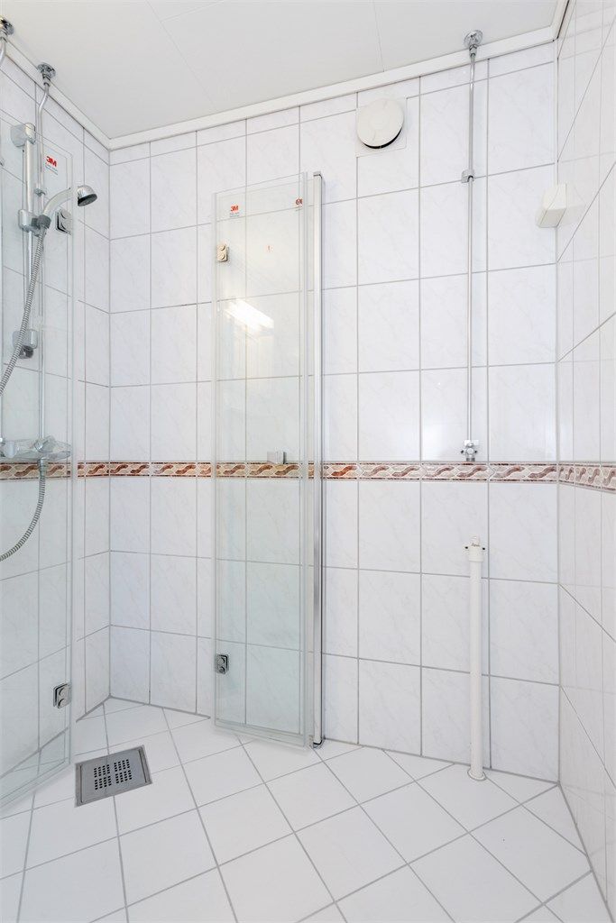 Dusjhjørne med innfellbare glassdører og flislagte overflater.
