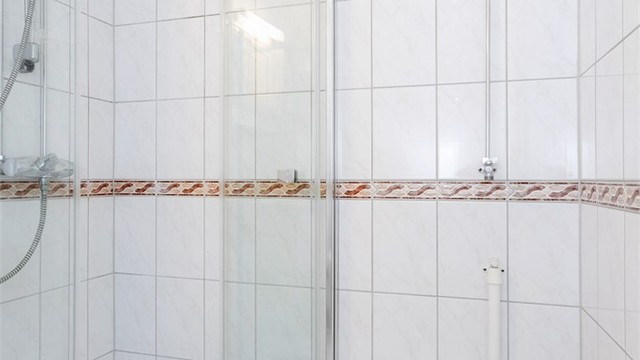 Dusjhjørne med innfellbare glassdører og flislagte overflater.