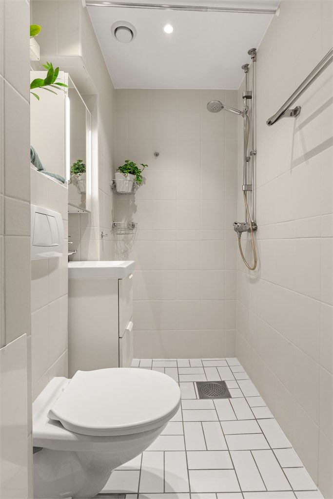 Badet er innredet med vegghengt toalett, servant med underskap og dusjhjørne.