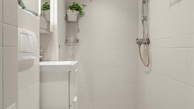 Badet er innredet med vegghengt toalett, servant med underskap og dusjhjørne.