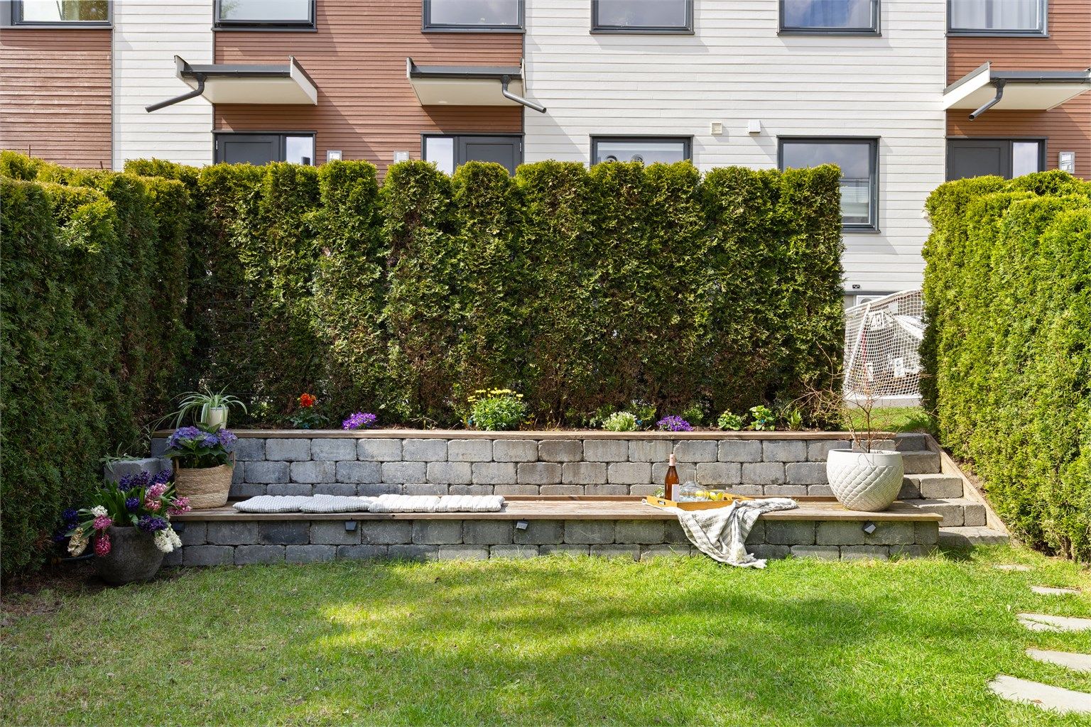 Pent opparbeidet uteplass med blomsterbed, sittebenk i naturstein med integrert belysning, og mulighet til å dekorere med planter og lykter.
