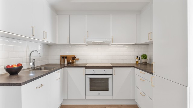 Kjøkkeninnredning med glatte fronter og laminat benkeplate med nedfelt vaskekum. Fliser og belysning over benkeplaten