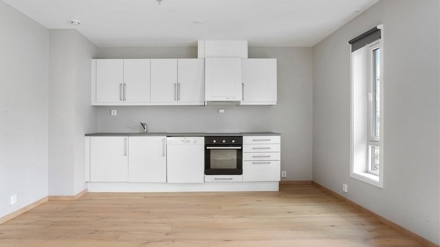 Kjøkkeninnredning fra byggeåret med slette, lyse fronter og laminatbenkeplate.