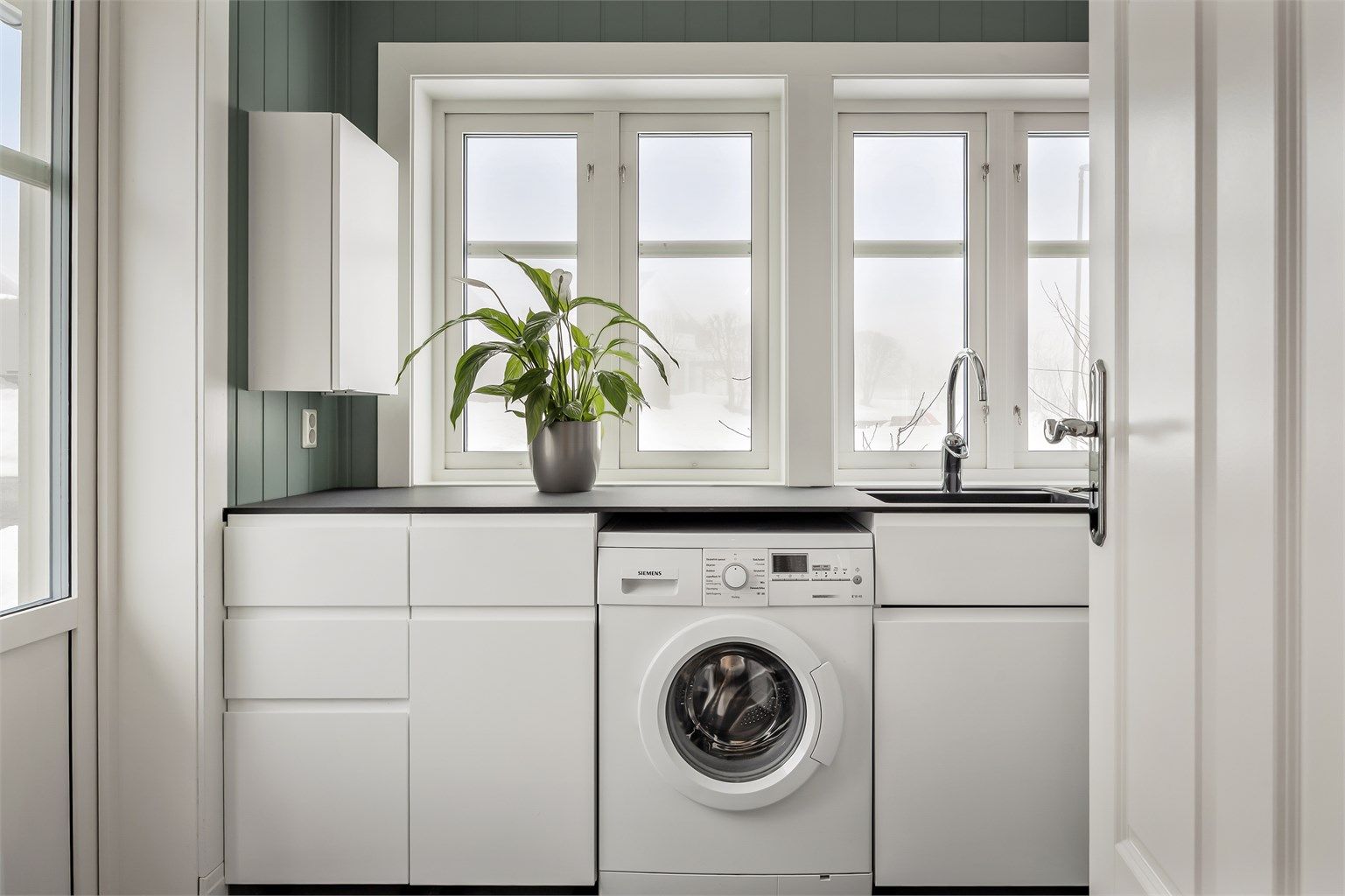 Praktisk vaskerom med egen inngang, skapinnredning, benkeplate i kompositt og opplegg for vaskemaskin.