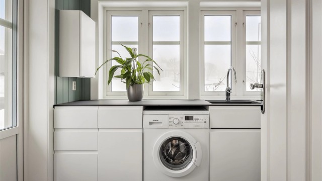 Praktisk vaskerom med egen inngang, skapinnredning, benkeplate i kompositt og opplegg for vaskemaskin.