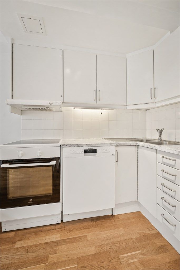 Fliser mellom kjøkkenbenk og overskap. Frittstående hvitevarer og ventilator i overskap.
