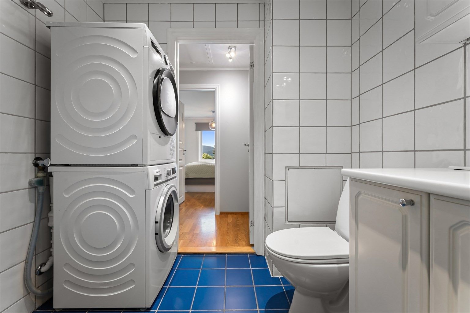 Badet har toalett, vegghengt servantinnredning, speil med overlys, dusjhjørne med dører og opplegg for vaskemaskin